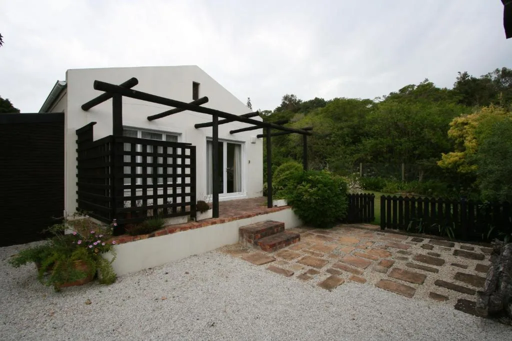 White cottage with black pergola and gravel courtyard surrounded by lush green vegetation