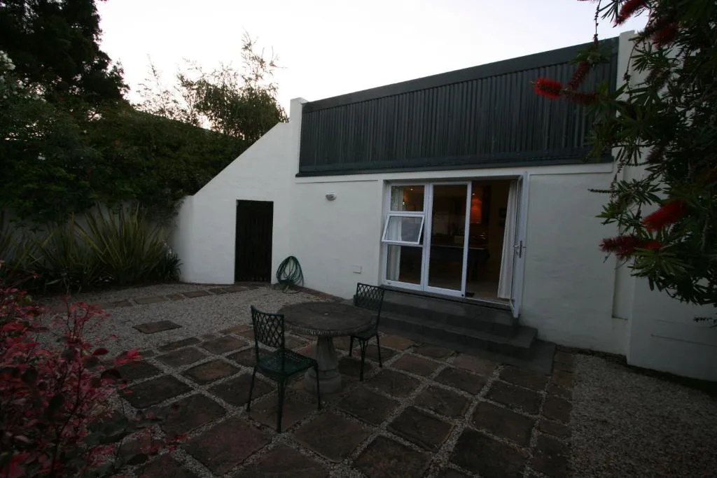 Modern white cottage with black roof and patio area, surrounded by lush greenery