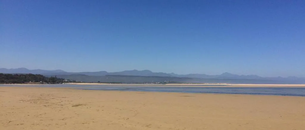 Wide sandy beach with mountains in the distance under clear blue sky