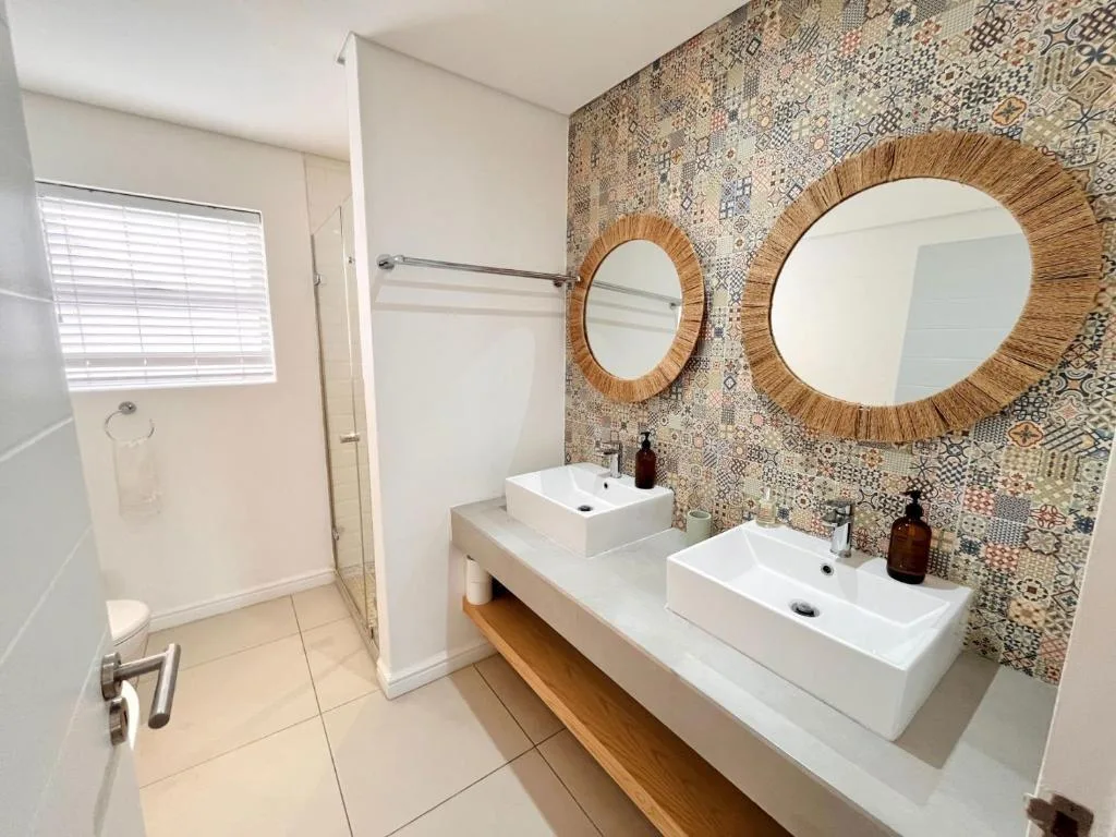 Modern bathroom with dual vessel sinks, patterned tile wall, wooden mirrors