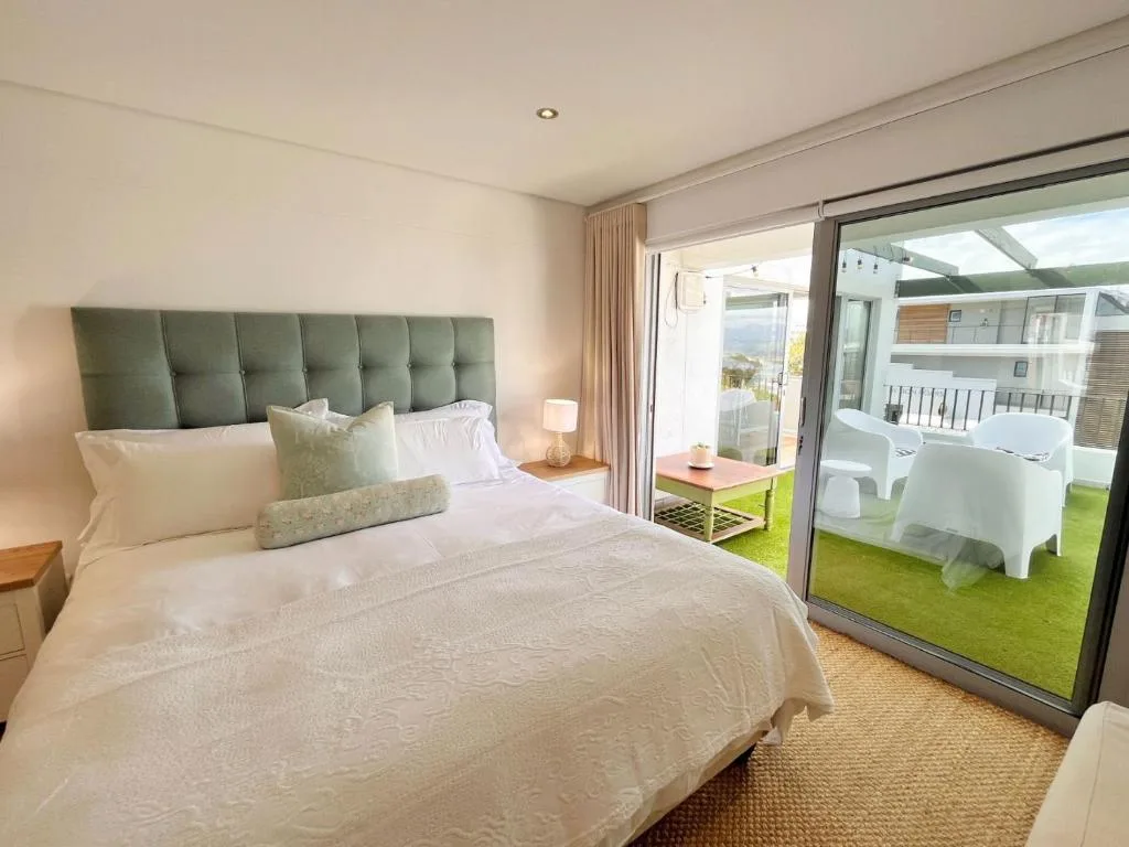 Spacious bedroom with green headboard, white bedding, and deck access