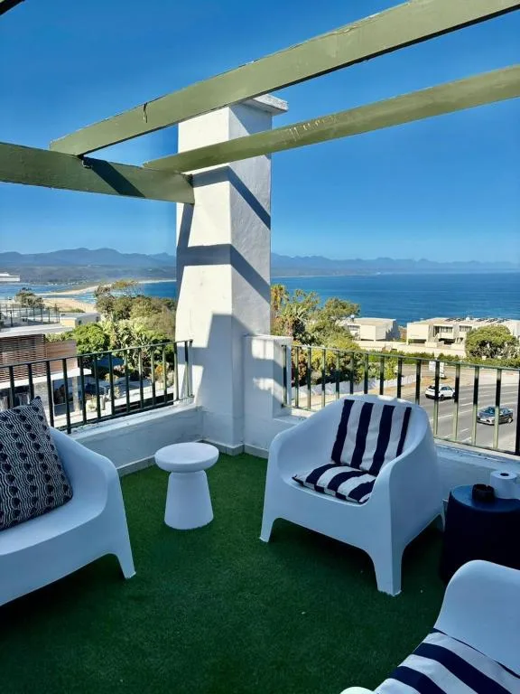 Elevated outdoor deck with white furniture and panoramic ocean and mountain views