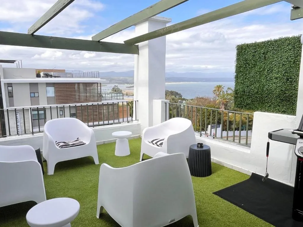 Elevated deck with white seating, ocean and mountain views, pergola shade structure