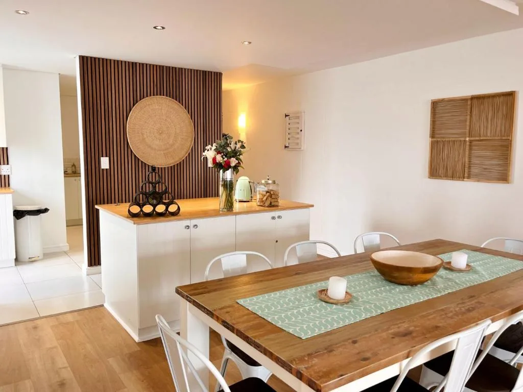 Modern dining room with wooden table, white chairs, and kitchen island beyond