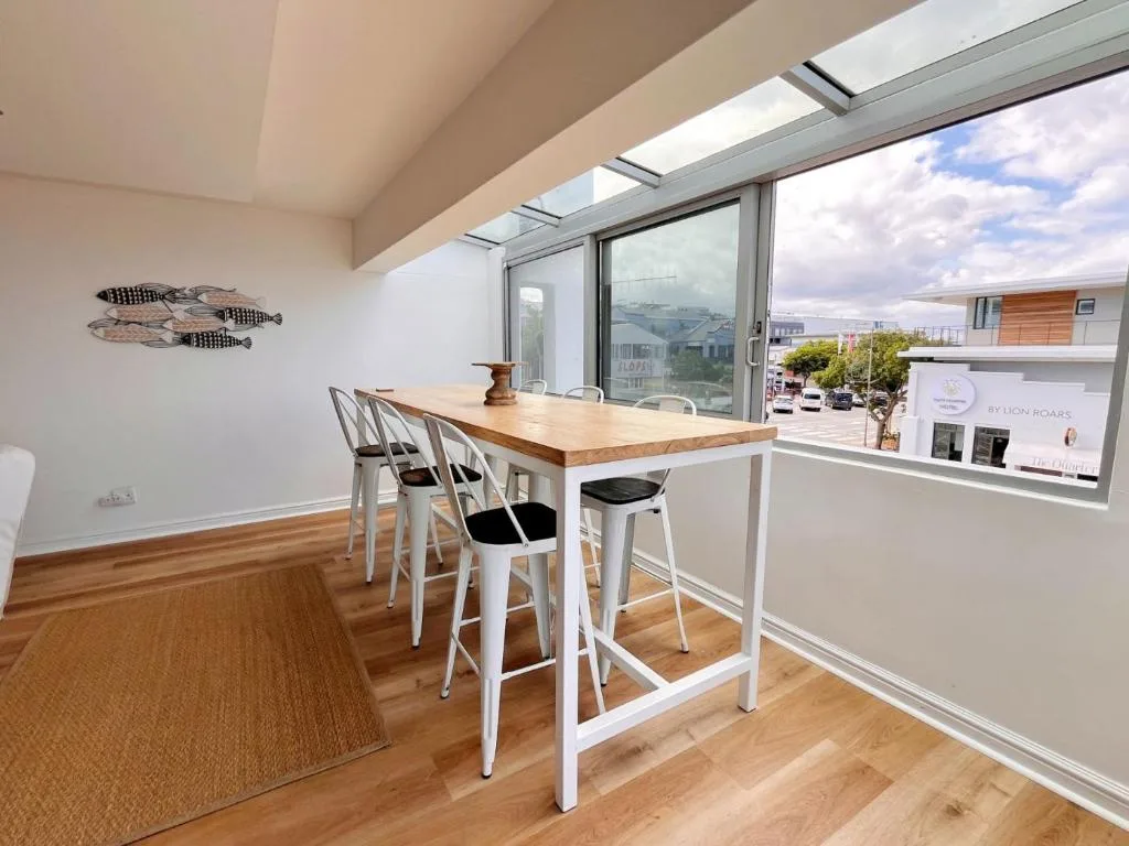 Modern dining area with wooden table, white bar stools, and panoramic mountain views