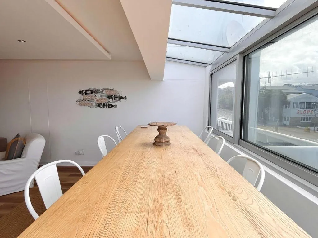 Long wooden dining table with white chairs in bright skylighted room