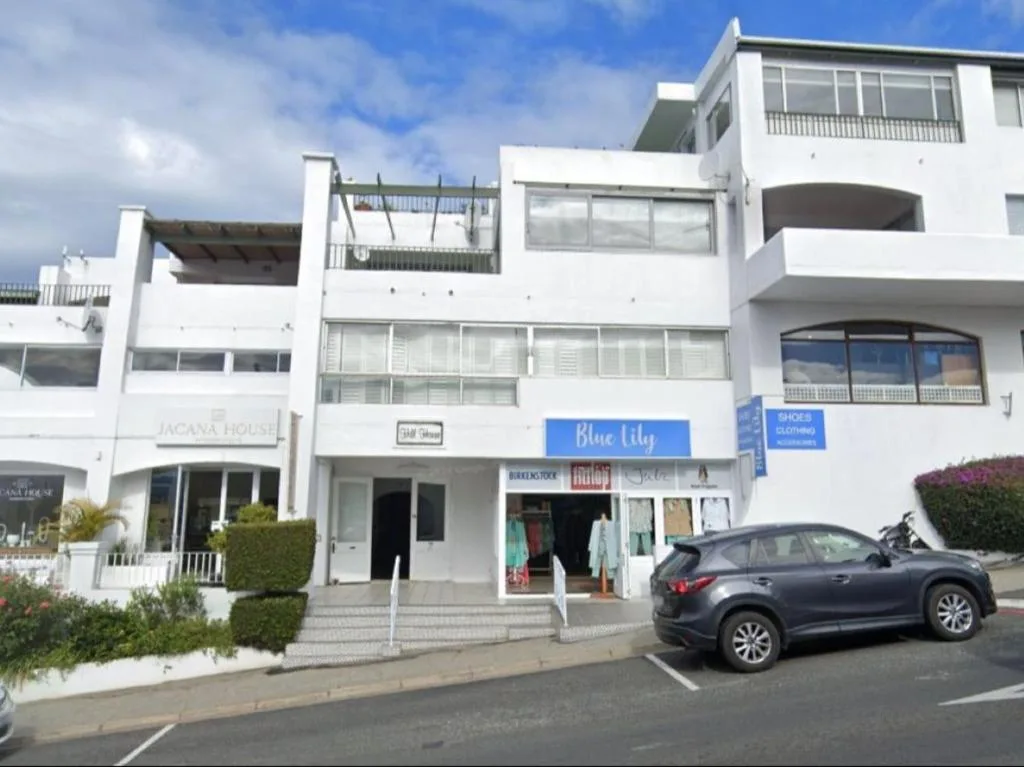 White modern apartment building facade with street-level shops and parked car