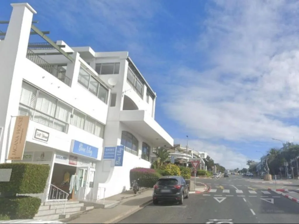 Modern white multi-story apartment building on street corner with shops