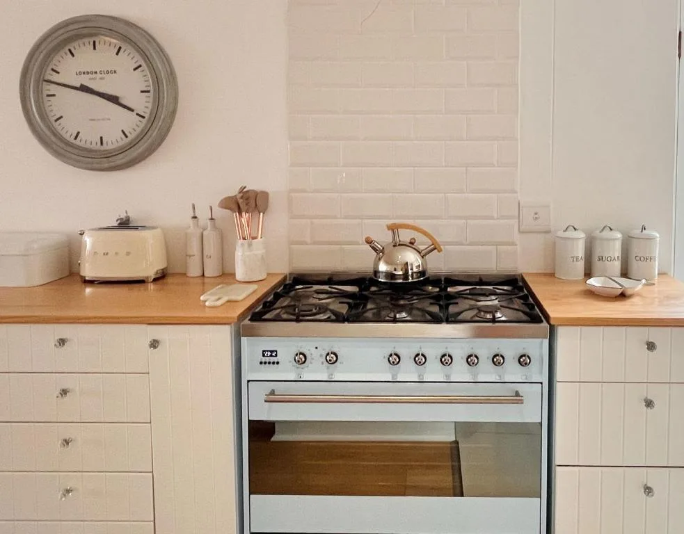Modern kitchen with gas stove, cream cabinetry, wooden countertop, and wall clock