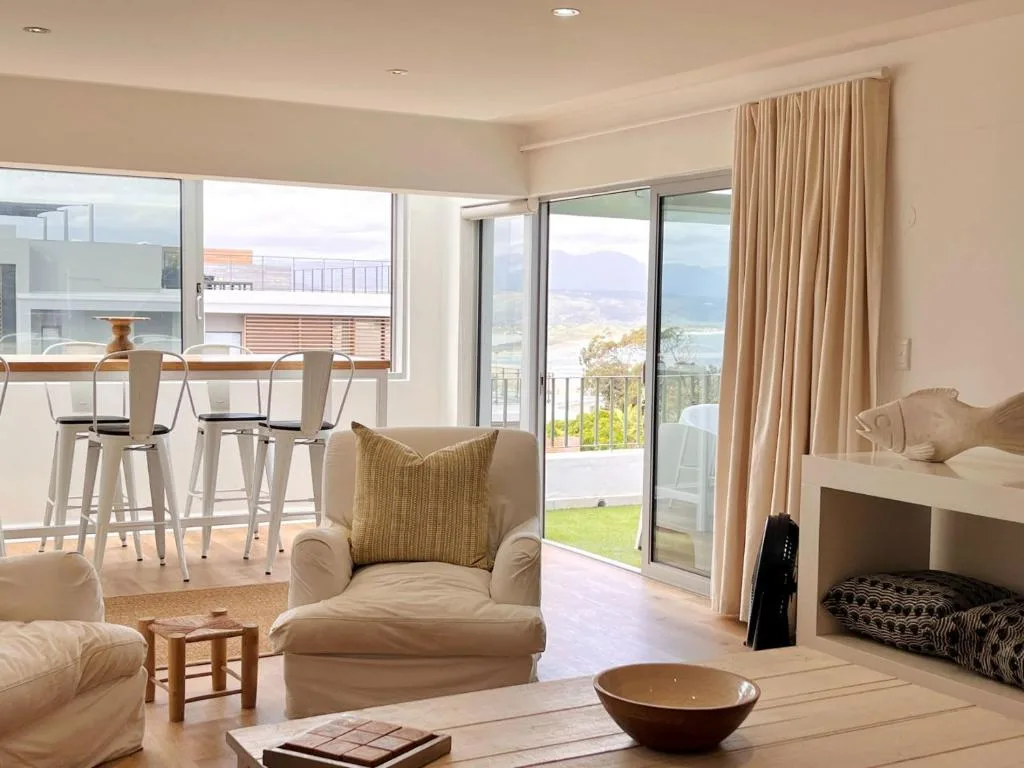 Bright open-plan lounge with cream armchair, ocean views through glass doors