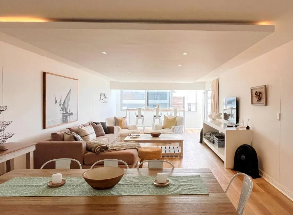 Spacious open-plan lounge with brown sofa, dining area, and ocean views through windows