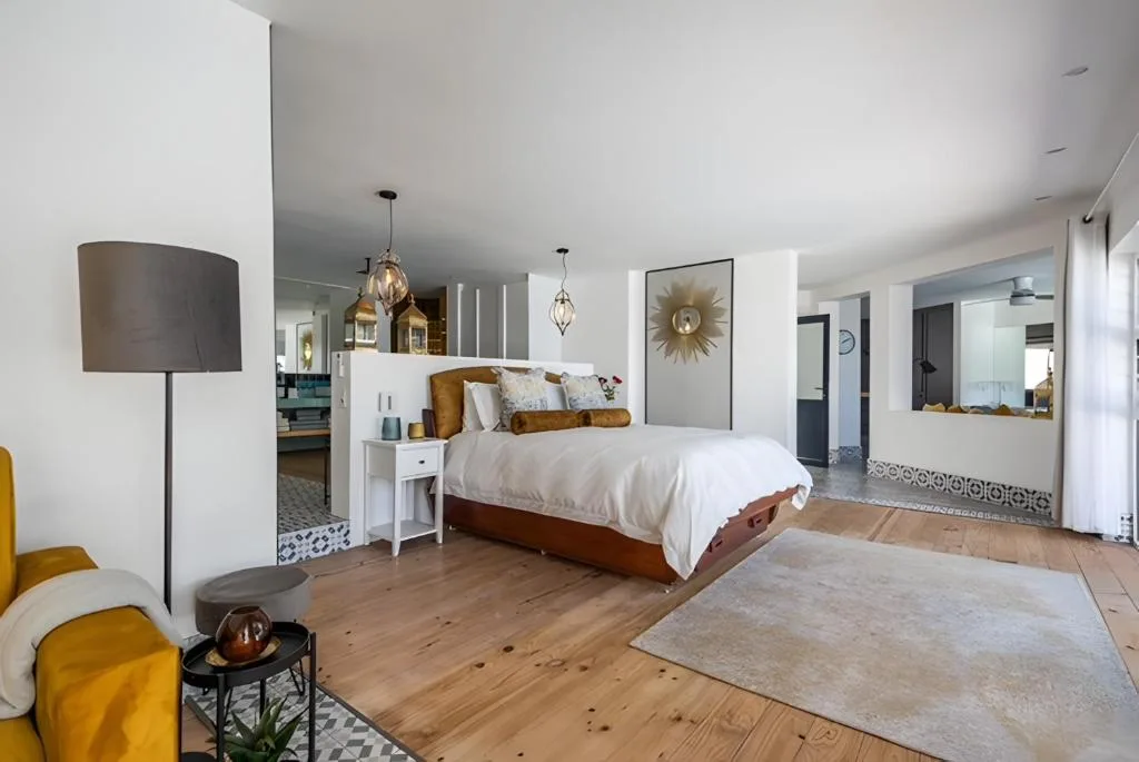 Spacious bedroom with wooden bed, white bedding, pendant lights, and ensuite bathroom