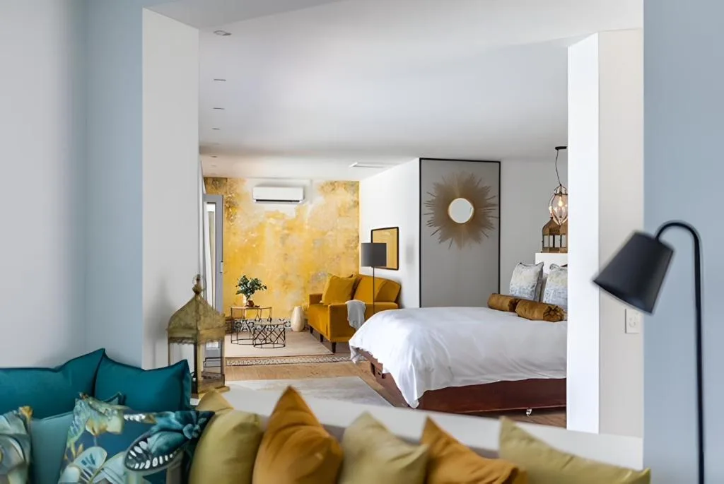 Bright modern bedroom with white bed, golden accents, and open-plan lounge area