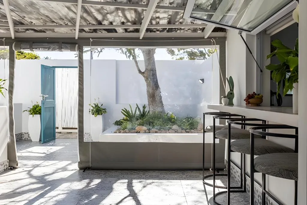 Modern covered patio with glass panels, seating, and garden views