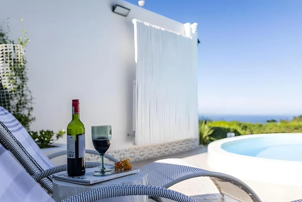 Outdoor deck with lounger, wine bottle, ocean view beyond white building