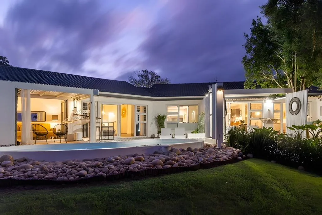 Modern white home with lit interior, wraparound deck, evening twilight view