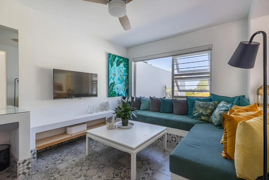 Modern living room with teal sofa, wall-mounted TV, and large windows