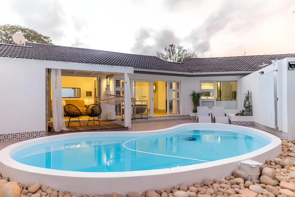 Oval swimming pool with white rim surrounded by pebbles and modern white house