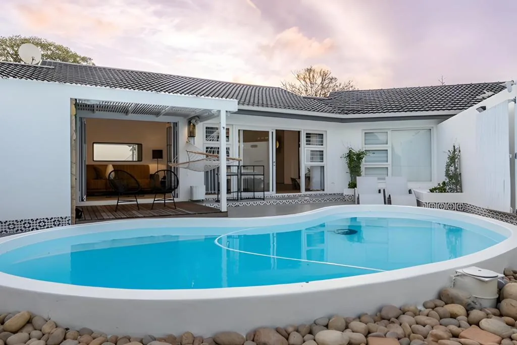 Oval swimming pool with white surround overlooking modern white holiday home