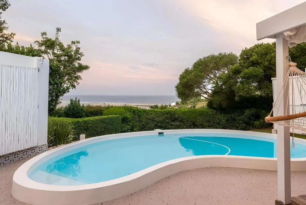 Curved swimming pool with ocean and coastal vegetation views beyond