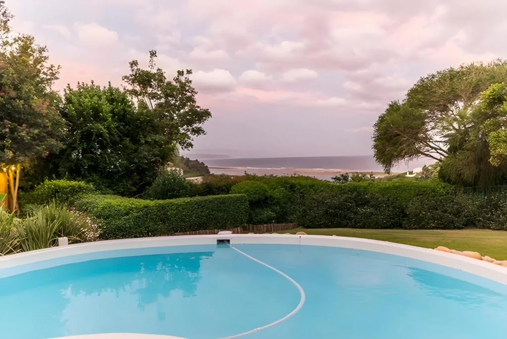 Round swimming pool with ocean and lagoon views beyond manicured gardens