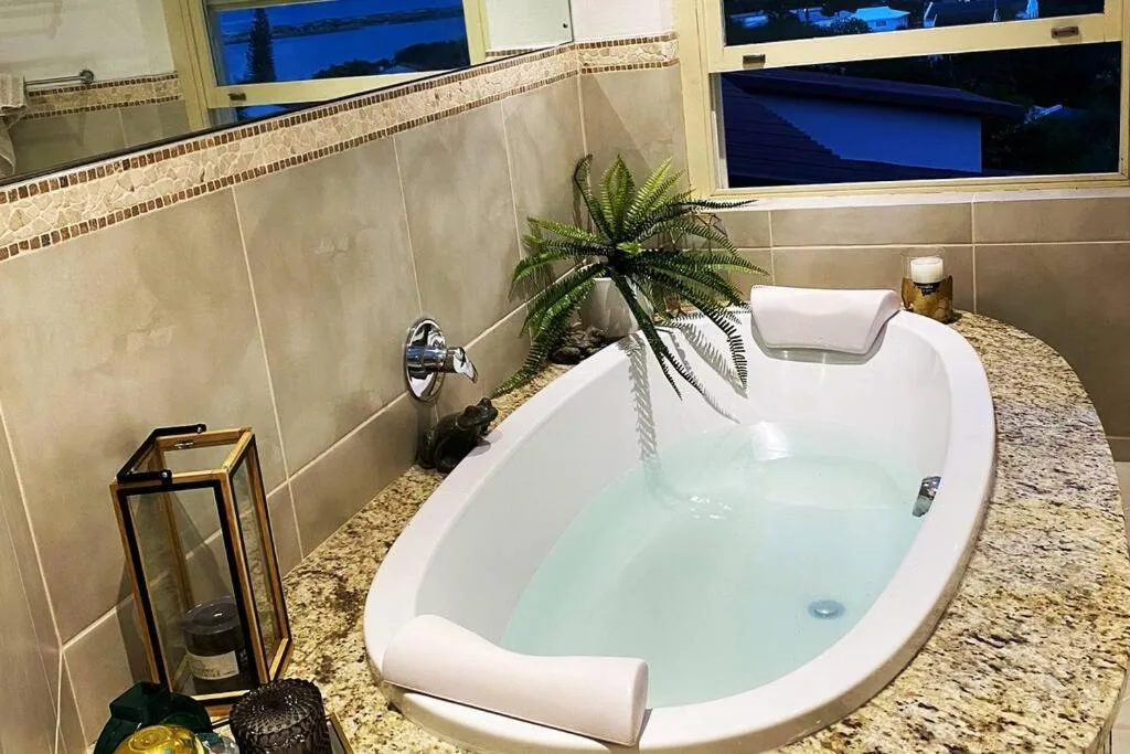 Luxurious white soaking tub with water jets and decorative fern plant
