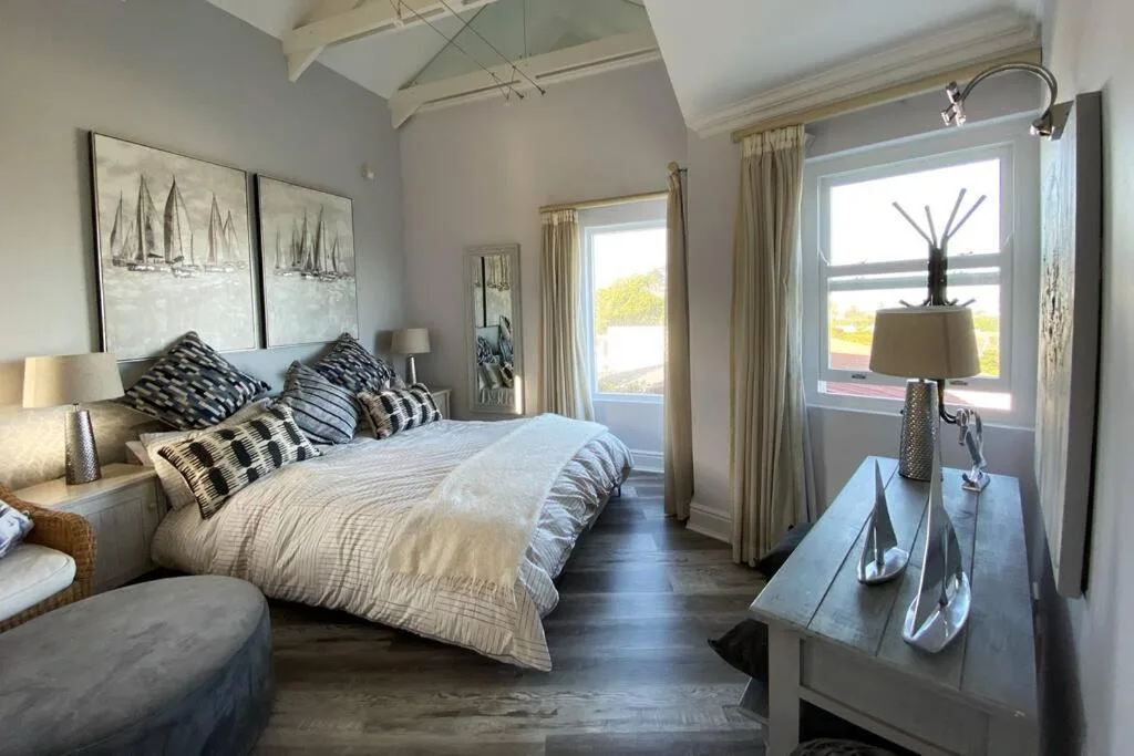 Spacious bedroom with queen bed, nautical artwork, and large windows overlooking the garden