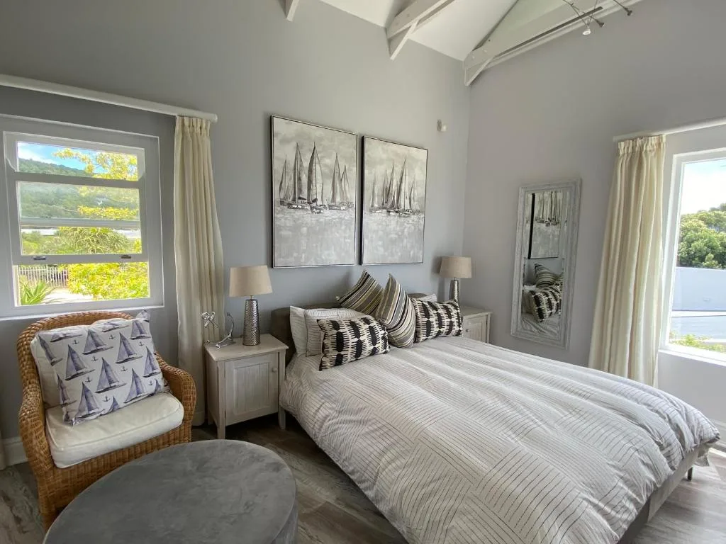 Bright bedroom with queen bed, wicker chair, and lagoon views through windows