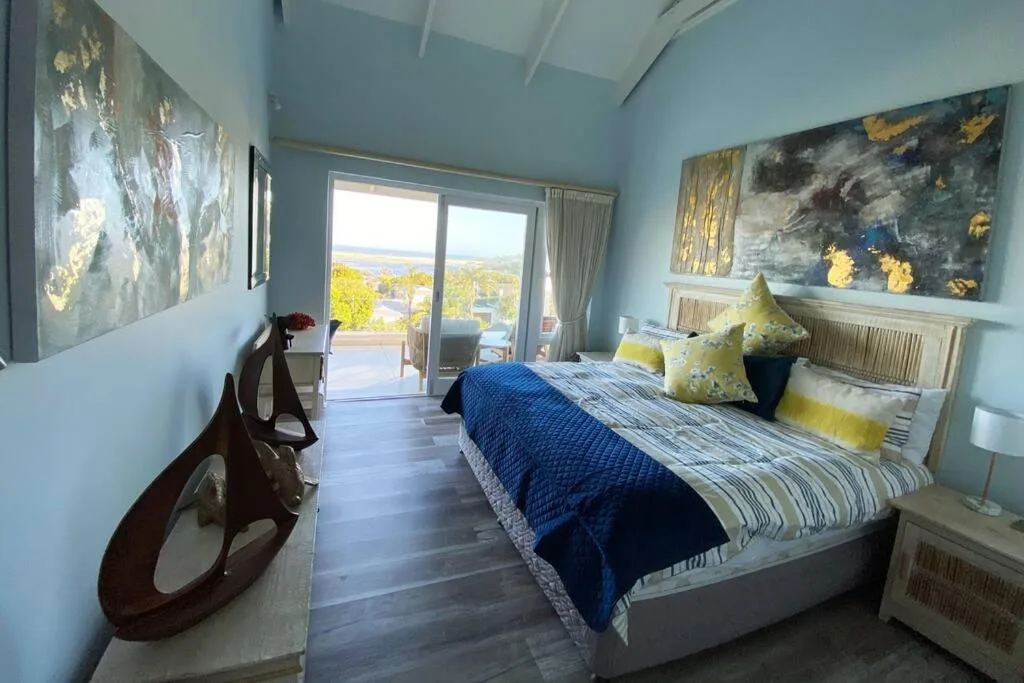 Spacious bedroom with blue bedding, yellow accents, and scenic views through sliding doors