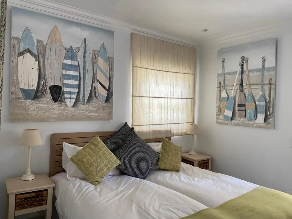 Bedroom with white bedding, green pillows, coastal artwork above headboard