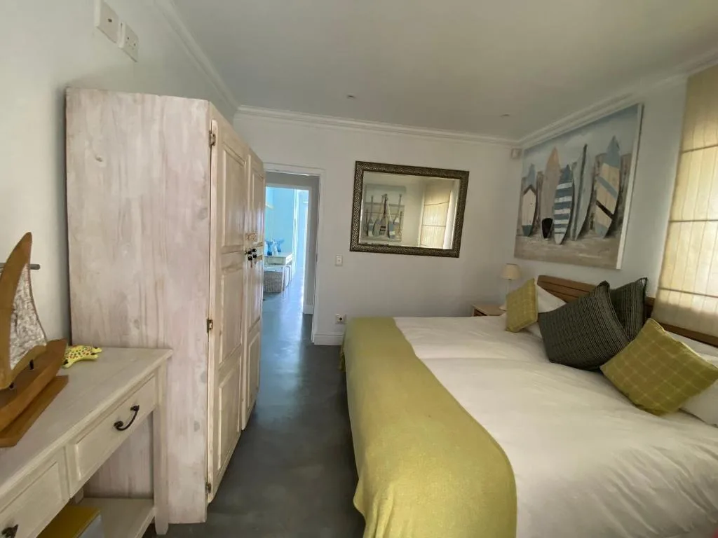 Bright bedroom with queen bed, yellow throw, and coastal decor artwork