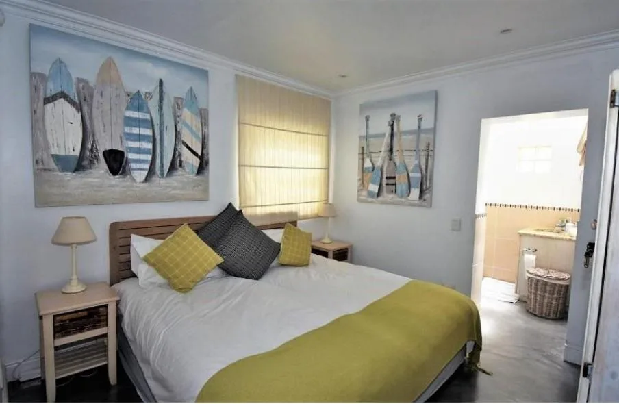 Bright bedroom with queen bed, yellow and black pillows, coastal artwork