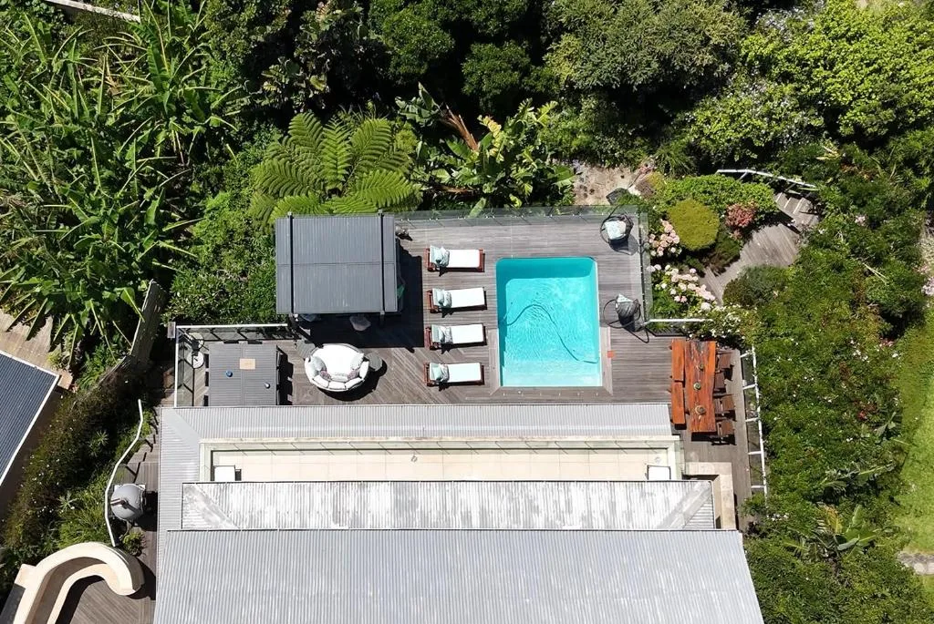 Aerial view of turquoise swimming pool on wooden deck surrounded by lush gardens