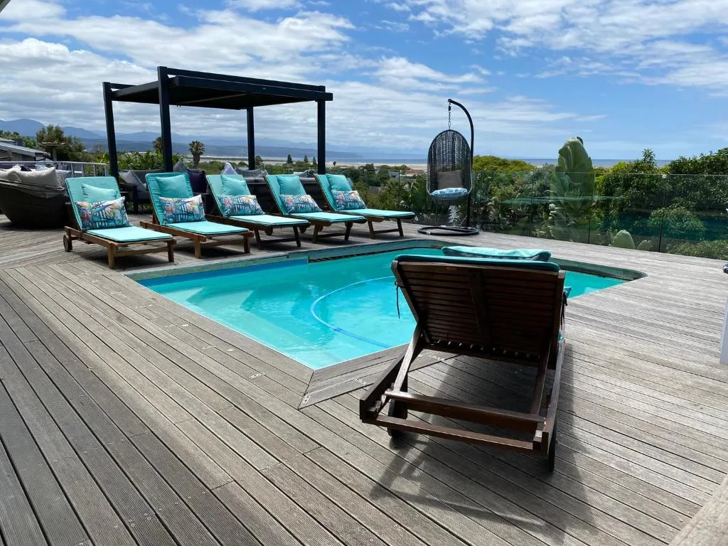 Turquoise swimming pool with loungers and mountain views on wooden deck