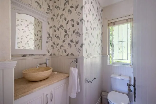 Modern bathroom with wooden vessel sink, white cabinetry, and botanical wallpaper