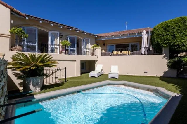 Sparkling swimming pool with loungers, facing modern house and manicured garden
