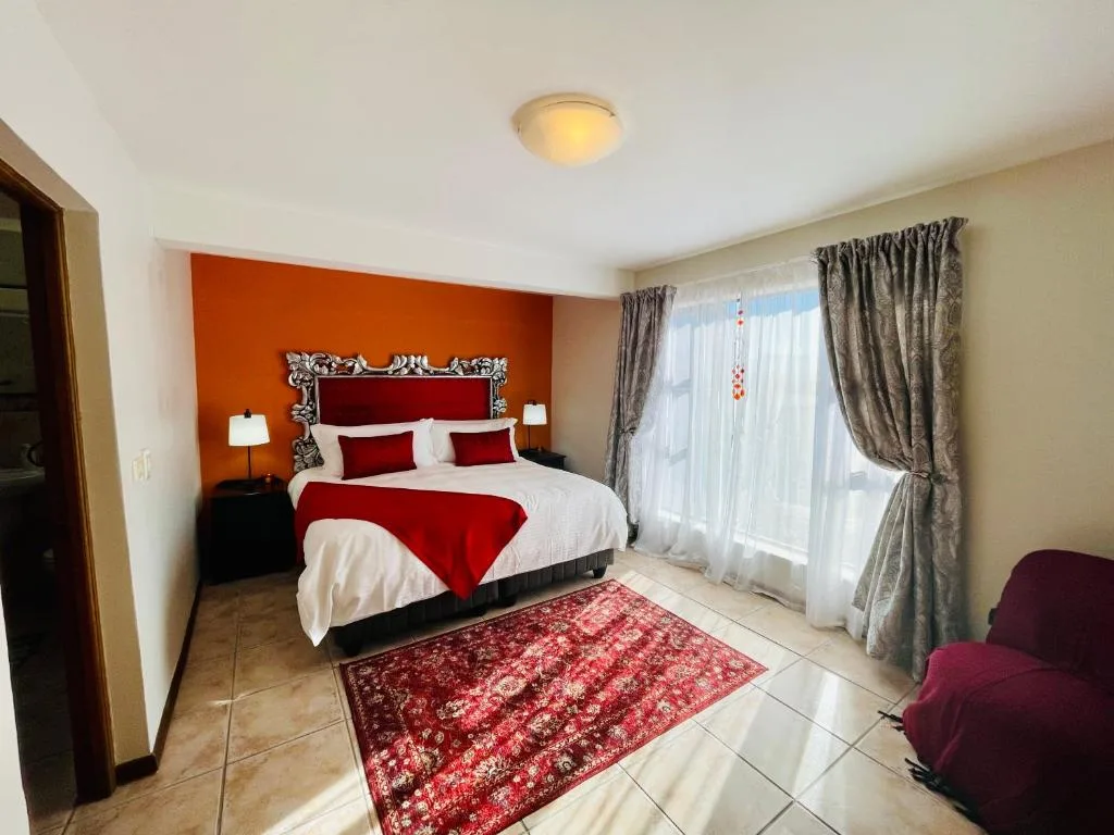 Spacious bedroom with red and white bedding, orange accent wall, and garden views