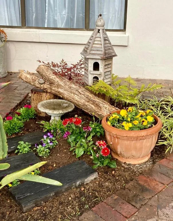 Garden courtyard with bird house, log, bird bath, and colorful flowering plants