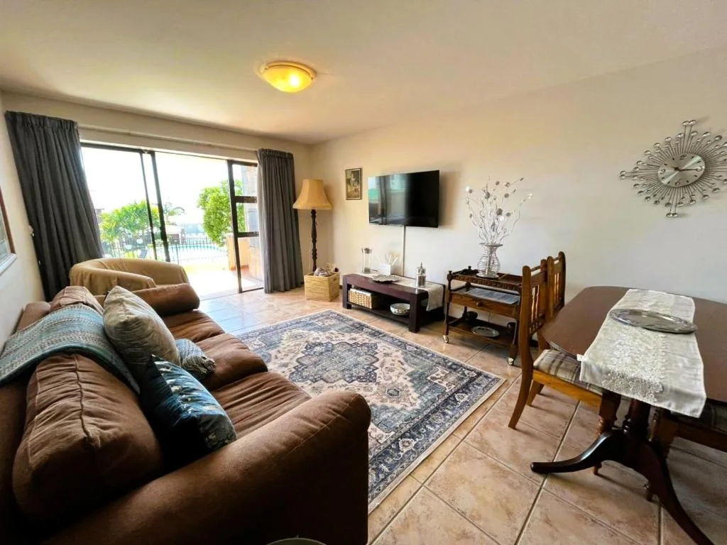 Spacious lounge with brown leather sofa, TV, and deck access overlooking garden