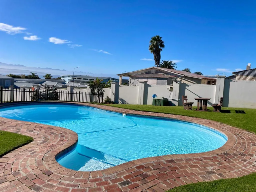 Curved swimming pool with brick patio and manicured lawn surrounded by property