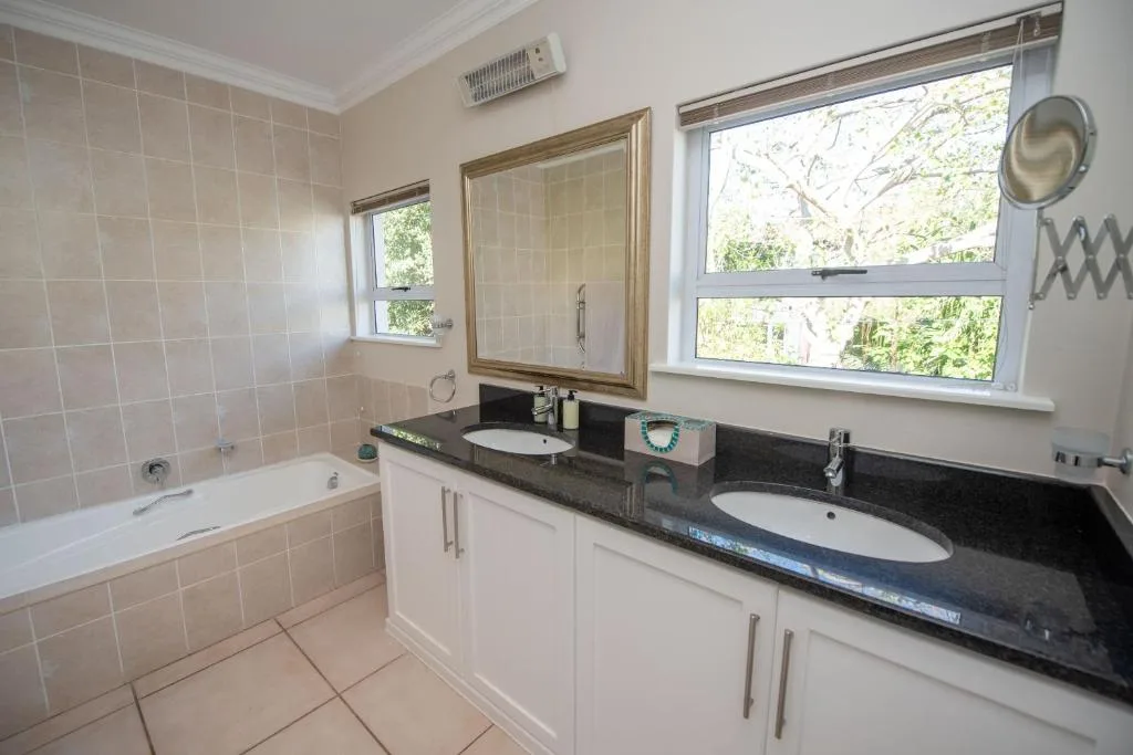 Bright bathroom with double vanity, dark countertop, bathtub, and large windows