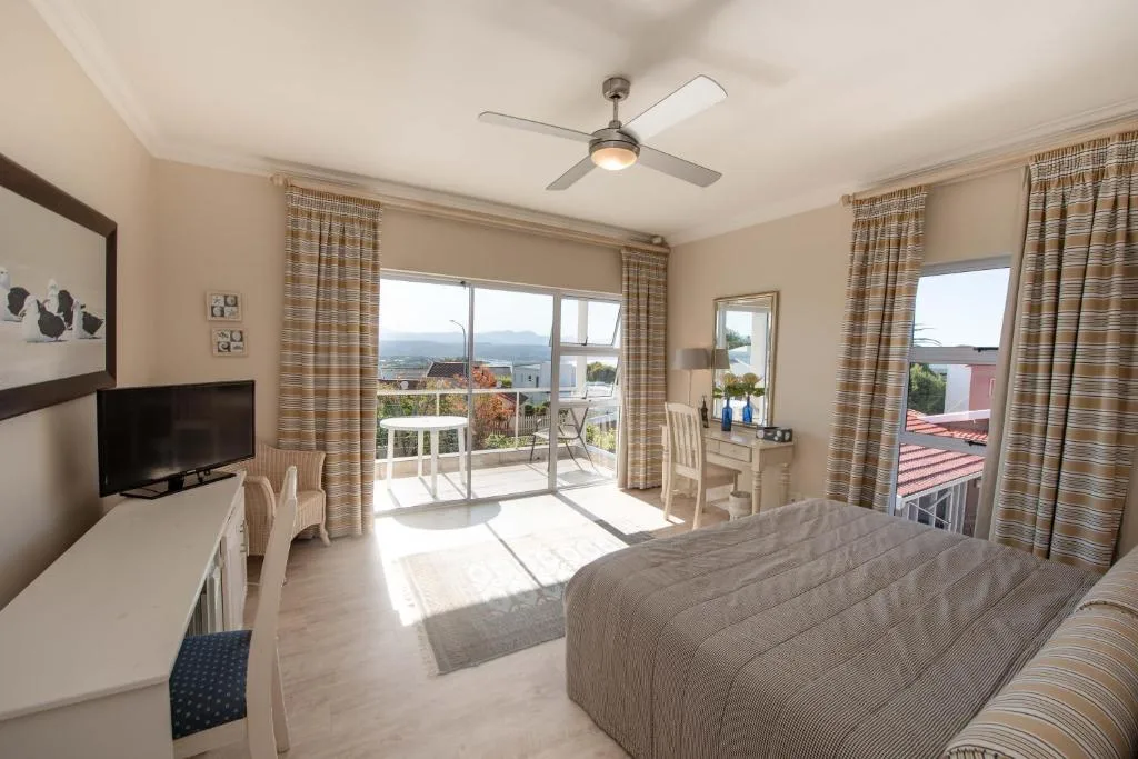 Spacious bedroom with bed, TV, ceiling fan, and mountain views through glass doors