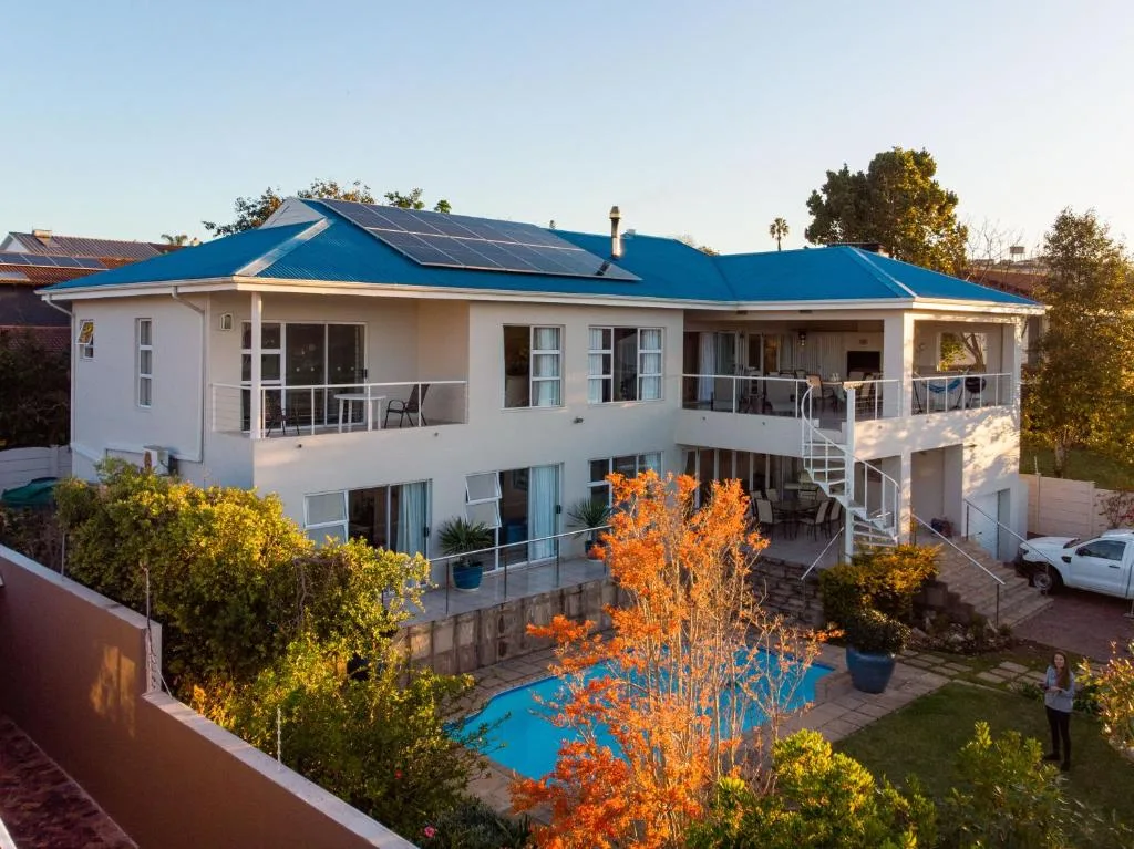Modern white house with blue roof and pool, garden surroundings visible
