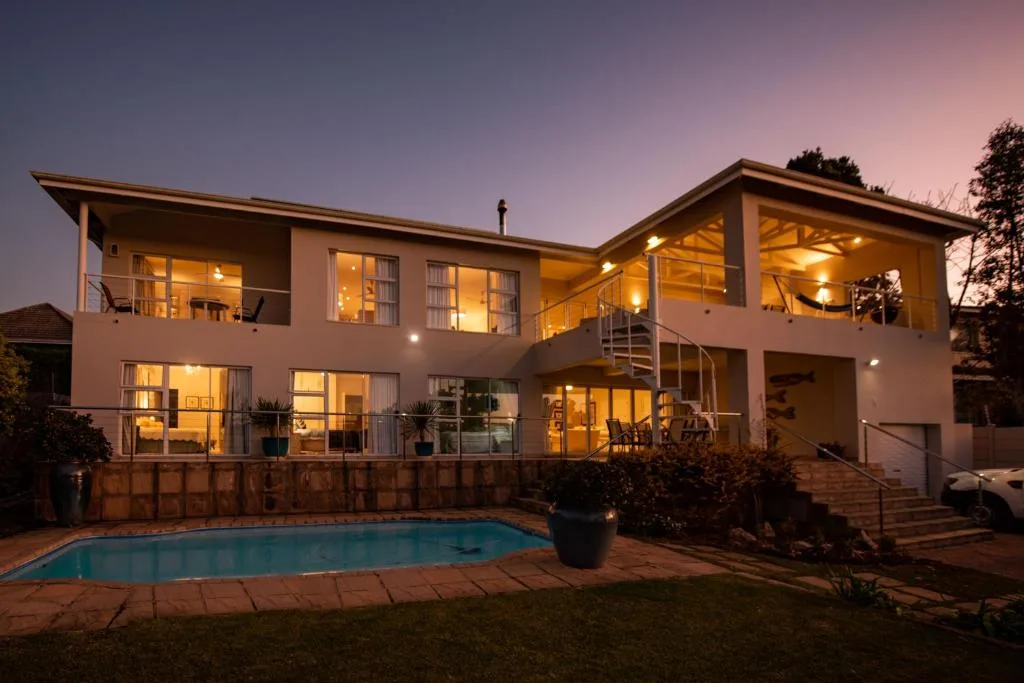 Modern two-story house illuminated at dusk with swimming pool in foreground