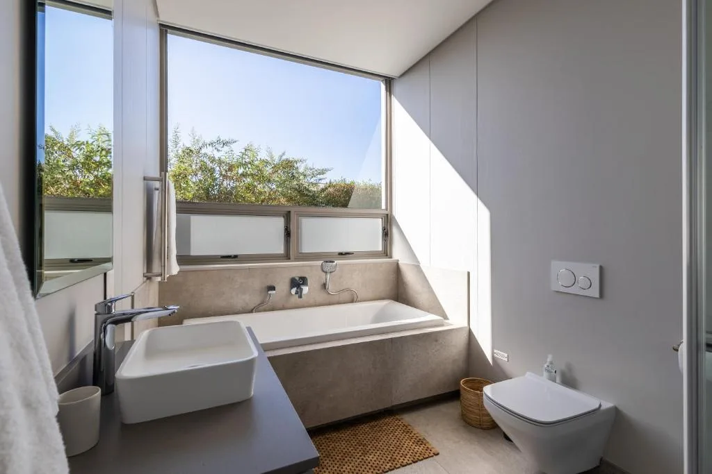 Modern bathroom with basin, bathtub, toilet, and large garden view windows