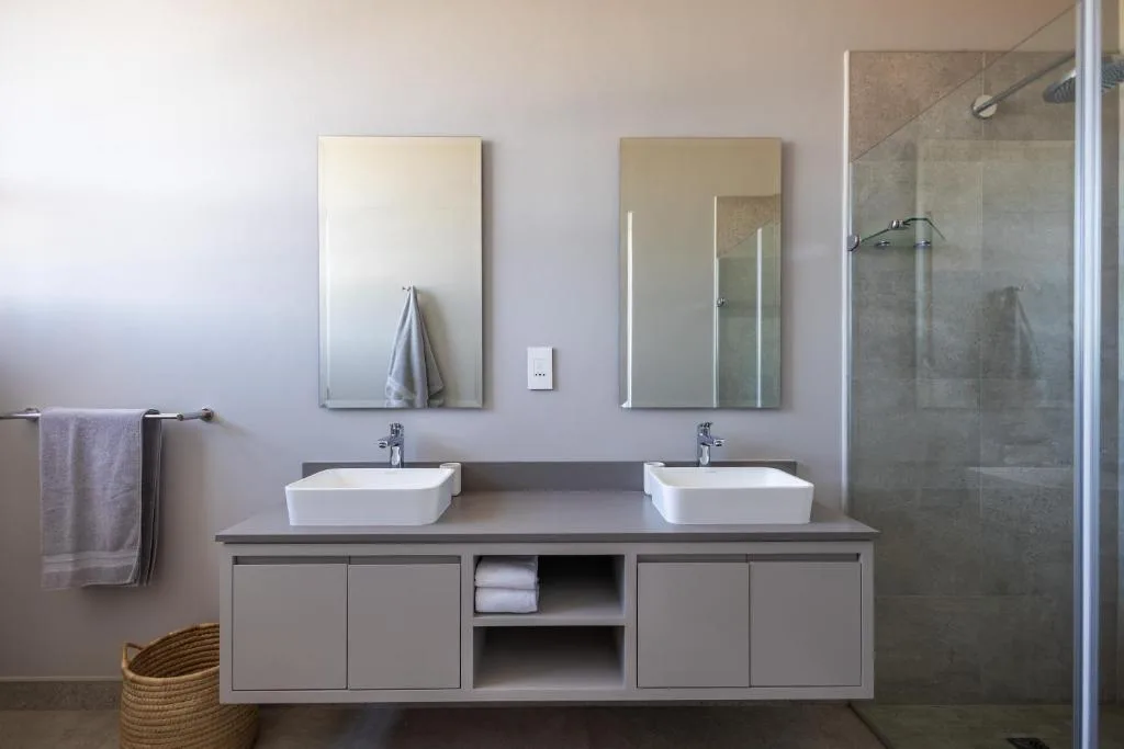 Modern dual-sink bathroom with illuminated mirrors and walk-in shower