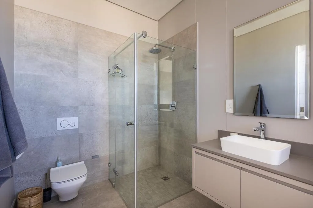 Modern bathroom with walk-in shower, white vessel sink, and illuminated mirror