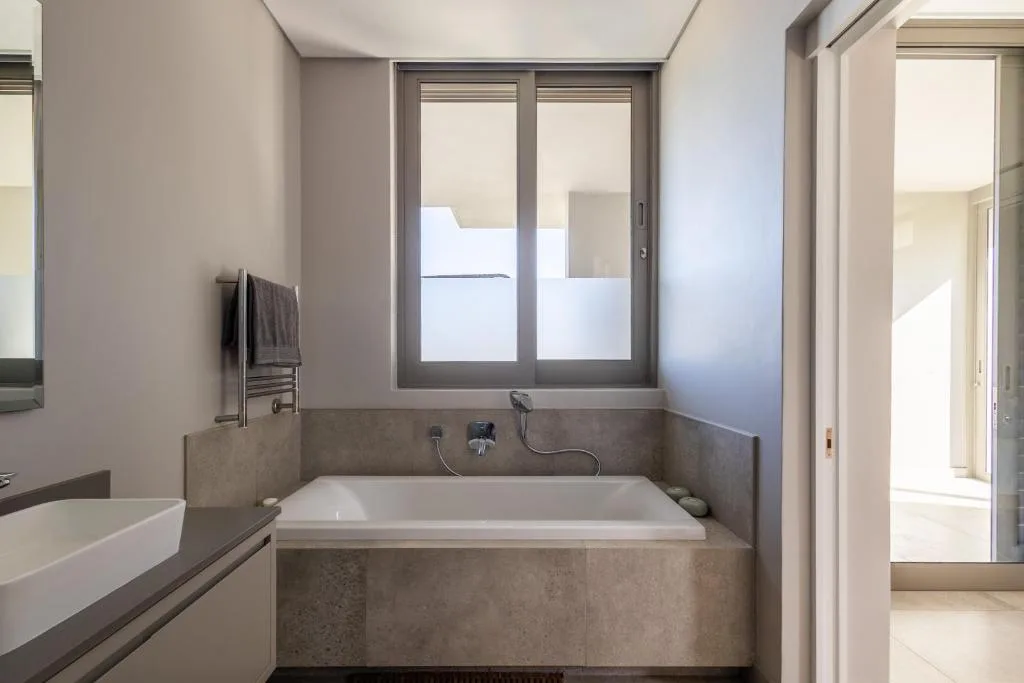 Modern bathroom with built-in bathtub, concrete finishes, and frosted window