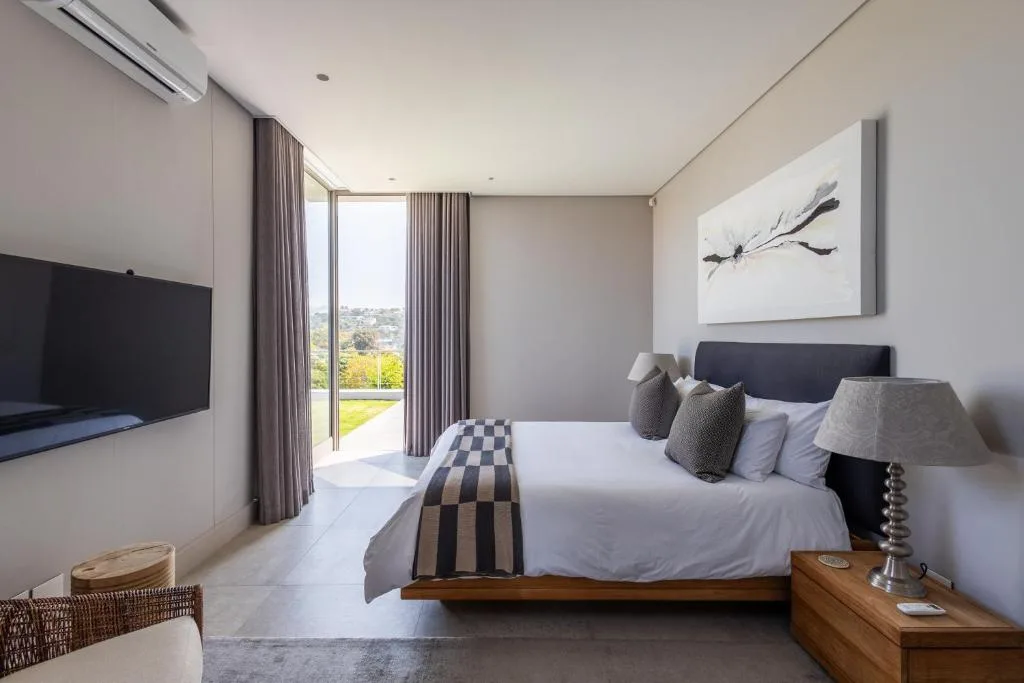 Modern bedroom with queen bed, wall art, TV, and garden views through glass doors