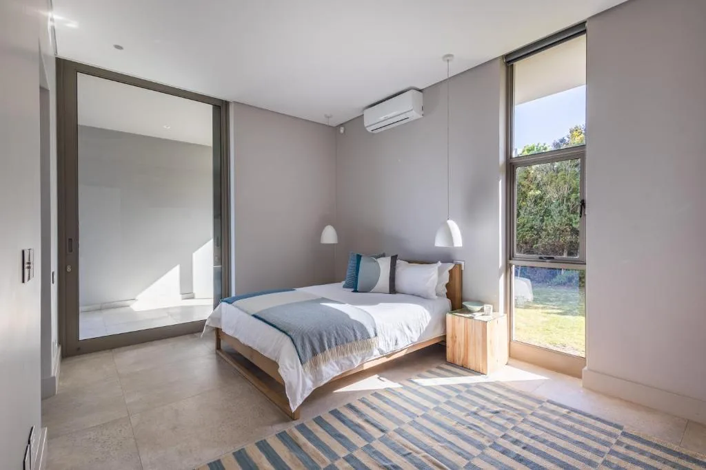 Modern bedroom with wooden bed, striped rug, garden views through large windows